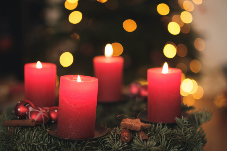 Adventskranz mit Kerzen und Weihnachtsbaum im Hintergrund