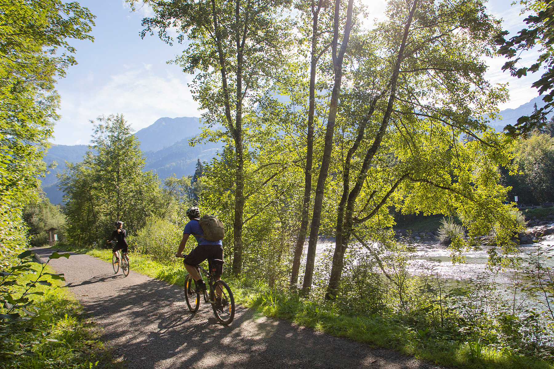 Zwei Radfahrer auf dem Radweg mit vielen Bäumen und einem Fluß im Allgäu